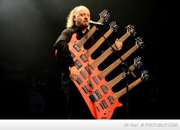 Bill Bailey playing his 6 neck guitar to an audience 